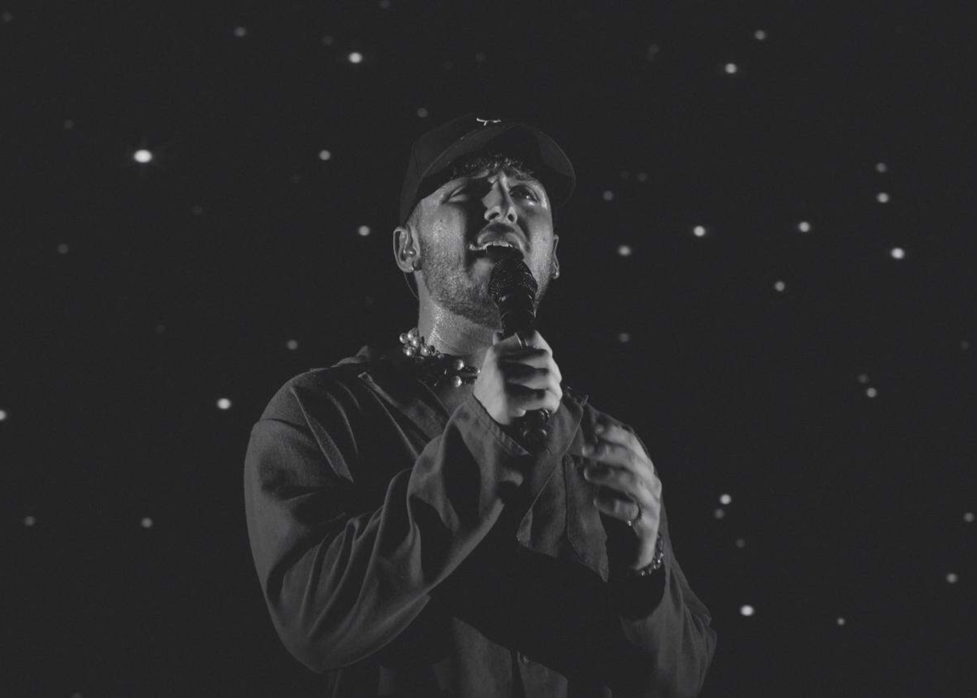 A grayscale photo of Andrew Bazzi holding a microphone while singing