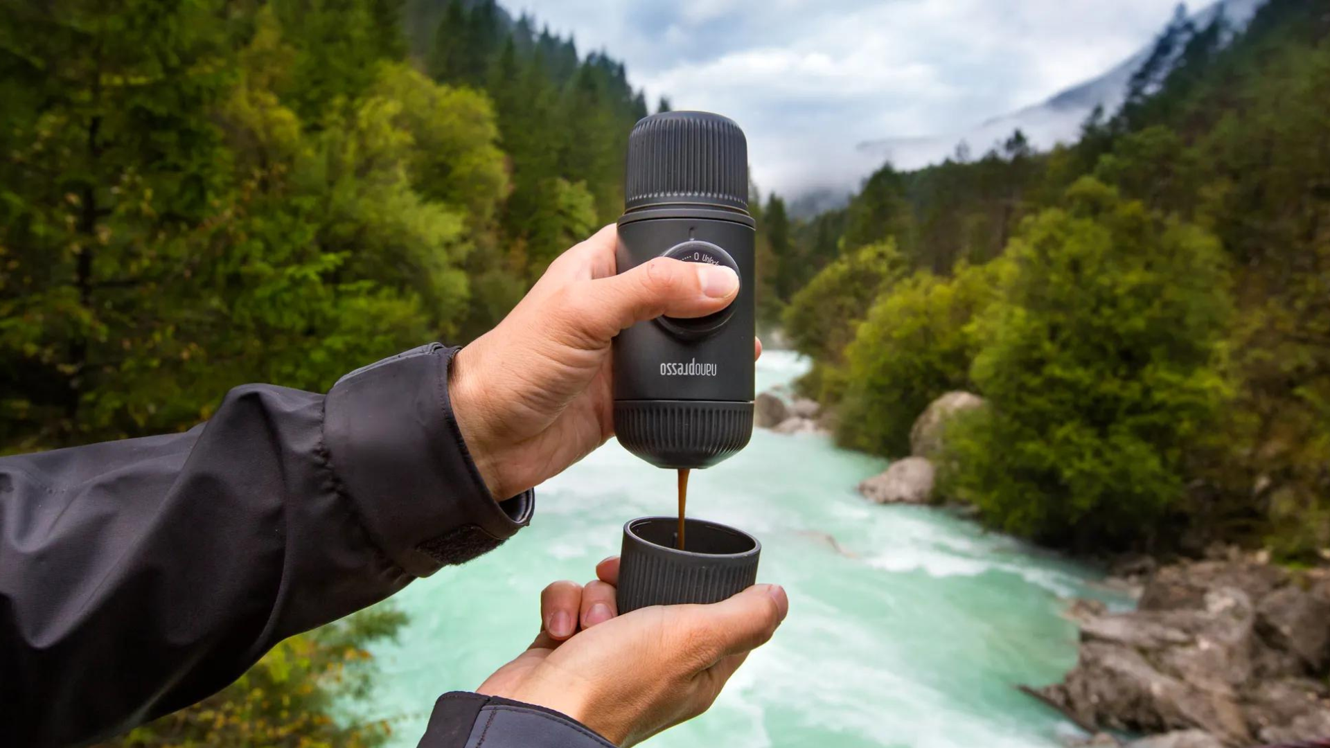 A man pouring coffee from a Nanopresso while in front of the river and trees