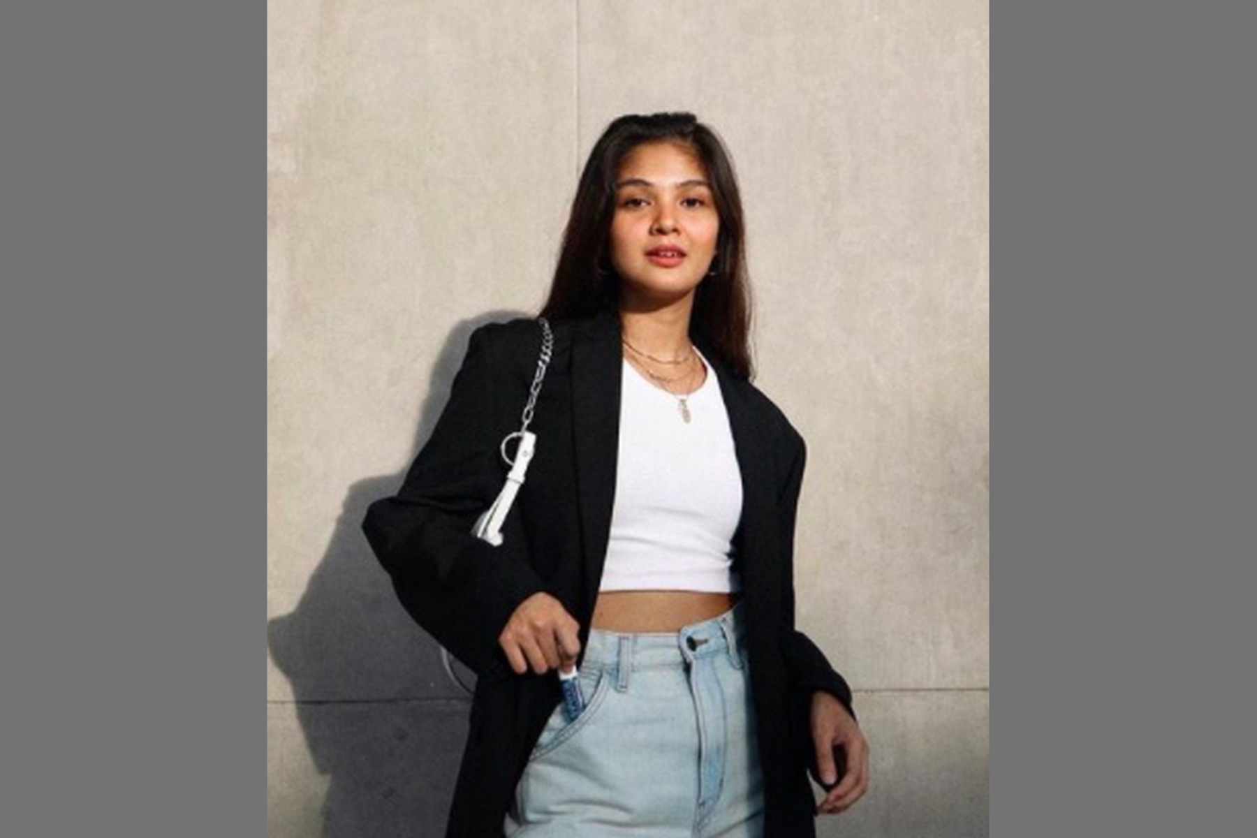 Angelique Manto wearing a professional attire on top of a white crop top while putting a lipstick on her pocket