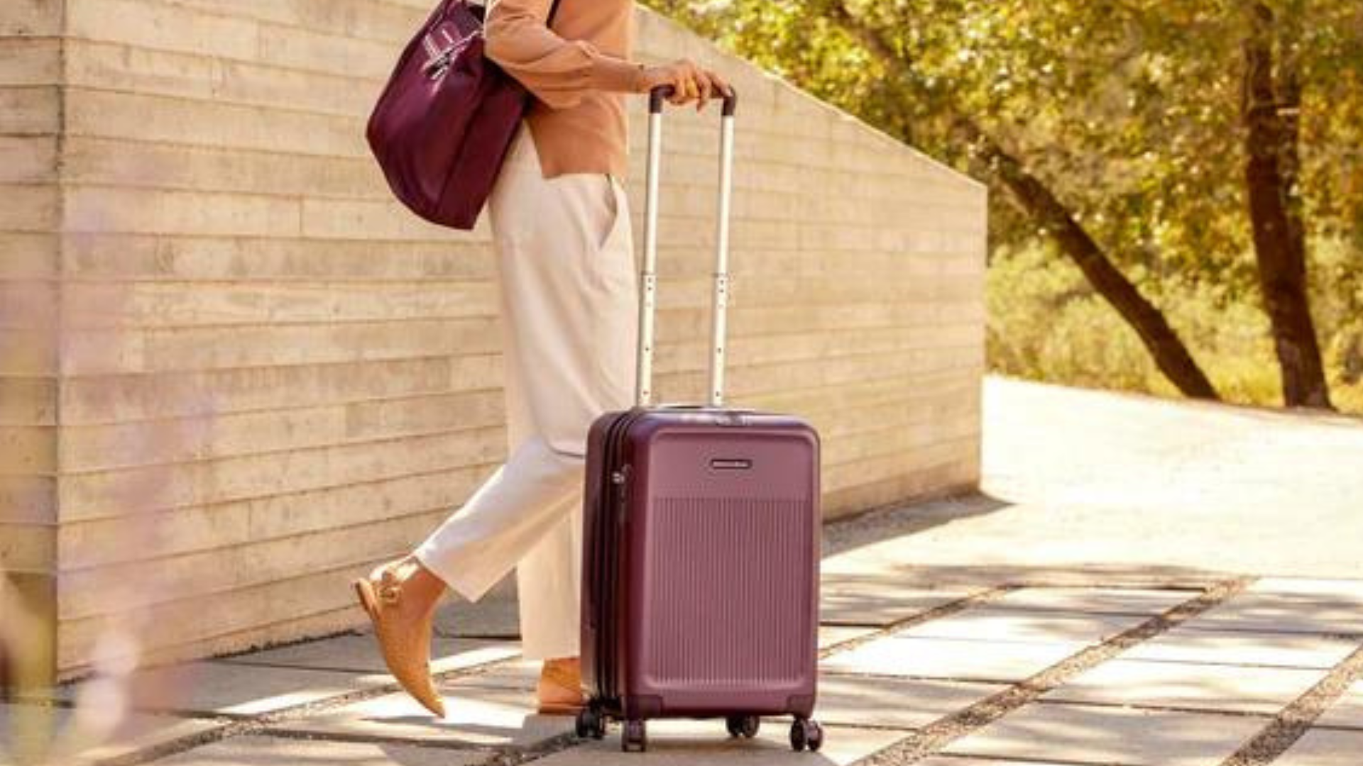A lady holding a maroon luggage while outdoors